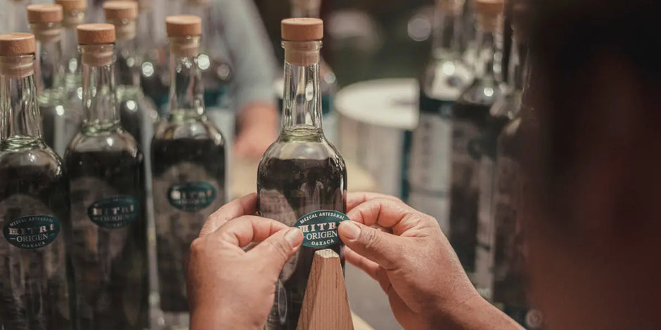 Proceso de envasado artesanal: colocación manual de etiqueta en botella de Mezcal Mitre Origen.