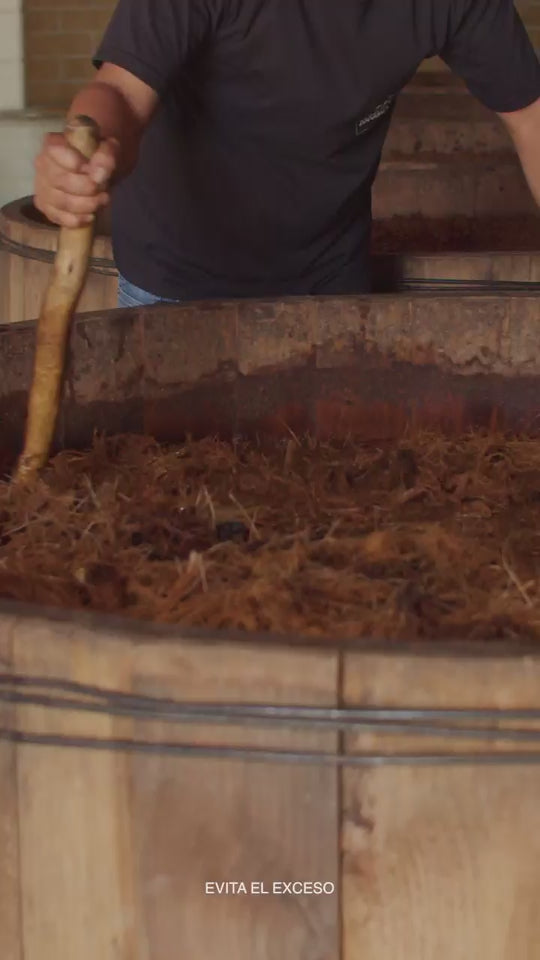 Proceso artesanal de fermentación del mezcal en tinas de madera, agitación manual tradicional.